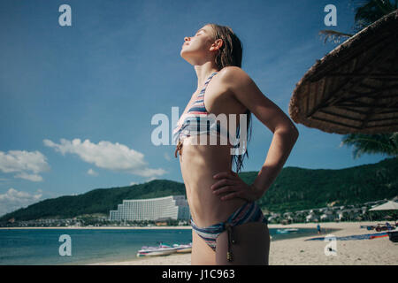 Caucasian donna che indossa un bikini godendo la luce del sole in spiaggia Foto Stock