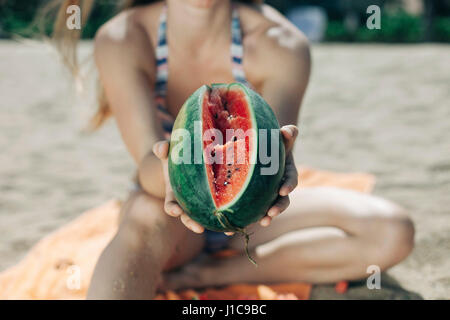 La donna caucasica mostra fette di cocomero sulla spiaggia Foto Stock