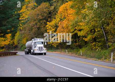 Classico bianco semi carrello rig con il serbatoio e la griglia di protezione e finestre a cabina alta sull'autostrada multi-lane road circondato da alberi di autunno Foto Stock