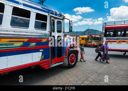 Antigua Guatemala - Aprile 19, 2014: Famiglia in un bus terminal con autobus colorati in Antigua, Guatemala Foto Stock