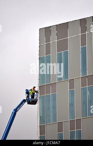 Operai in una cherry picker platform lavorando su un edificio moderno. Foto Stock