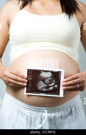 Un colpo di una donna in stato di gravidanza tenendo la sua scansione a ultrasuoni del suo bambino Foto Stock