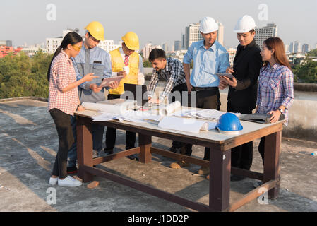 Bello ingegnere asiatici guardare il computer portatile con il lavoro di squadra e di architetti assetto di planata a un sito in costruzione Foto Stock