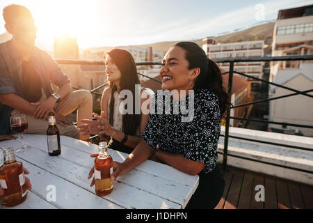 Sorridente giovane donna avente una parte sul tetto con gli amici. Amici raccolta sul tetto. Foto Stock