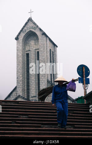 Un contadino cammina per le operazioni al di fuori della chiesa di pietra in Sa Pa (Sapa), nel Vietnam del nord, sud-est asiatico Foto Stock