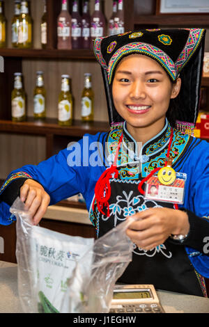 Guizhou, Cina. Han giovane donna cinese in abito Bouyei, lavorando in una banchina di riposo. Foto Stock