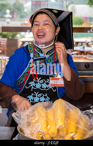 Guizhou, Cina. Han giovane donna cinese in abito Bouyei, lavorando in una banchina di riposo. Foto Stock