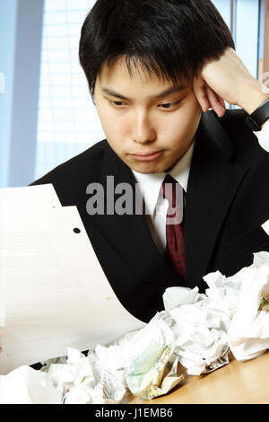 Un colpo di un sottolineato imprenditore asiatico lavorando duro in ufficio con la carta su tutto il tavolo Foto Stock
