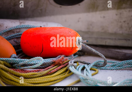 Rosso brillante boa di sicurezza poggia su dolcemente avvolto ad anello funi a bordo della barca da pesca per la sicurezza in movimento da aree marine e proteggere la barca da eventuali danni Foto Stock