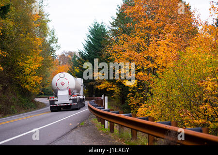 Grande classico Carrello con cisterna rimorchio per il trasporto di gas naturale liquefatto a turno della strada tortuosa con recinzione metallica e linee di divisione Foto Stock