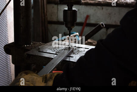 Operaio edile trapani foro nello stelo di ferro metallico mediante trapano industriale in un workshop scuro / workshed / factory Foto Stock