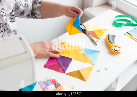 Ricamo e la trapuntatura in officina di una donna sarto su sfondo bianco - Mani di adattare la donna a lavorare con pezzi di tessuto colorato sul tavolo con fili, tessuti, aghi, taglierine. Foto Stock