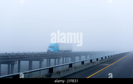 Modern big blue rig semi-carrello con un rimorchio dotato di luci sul cargo trasporta su un lungo viadotto in calcestruzzo sul burrone su supporti in autostrada Foto Stock