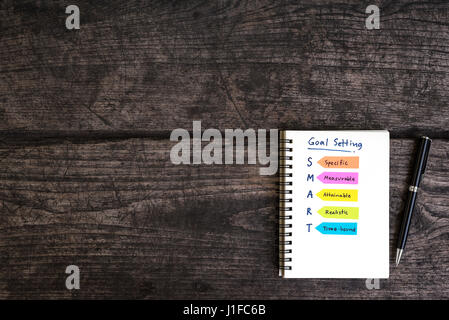 La grafia impostazione obiettivo smart il notebook aperto con la penna sulla grungy scrivania in legno, la concezione di business Foto Stock