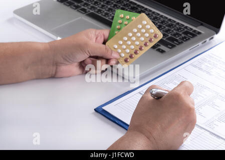 Medico mano che tiene il controllo delle nascite pillole e la penna sul computer e la storia del paziente forma sul tavolo bianco, healthcare, la farmacia e la medicina concept Foto Stock