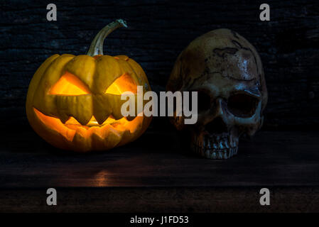 Zucca di Halloween jack testa lanterna con scary male volti e cranio umano su sfondo di legno nelle tenebre della notte Foto Stock