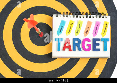 Dart in target bullseye con parole bersaglio sul notebook con scrittura realizzabile tempestivamente gli obiettivi pertinenti l'istruzione al lavoro di squadra oltre dartboard backgrou Foto Stock