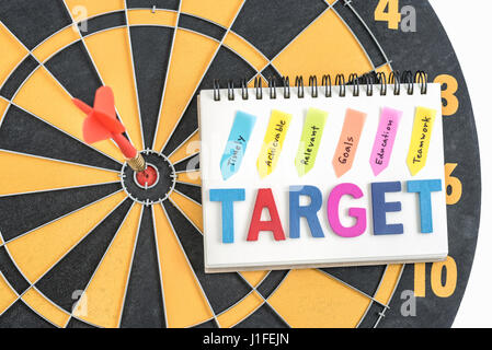 Dart in target bullseye con parole bersaglio sul notebook con scrittura realizzabile tempestivamente gli obiettivi pertinenti l'istruzione al lavoro di squadra oltre dartboard backgrou Foto Stock