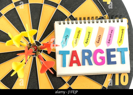 Sei in dart bullseye con parole bersaglio sul notebook con scrittura realizzabile tempestivamente gli obiettivi pertinenti istruzione teamwork su sfondo dartboard, Foto Stock