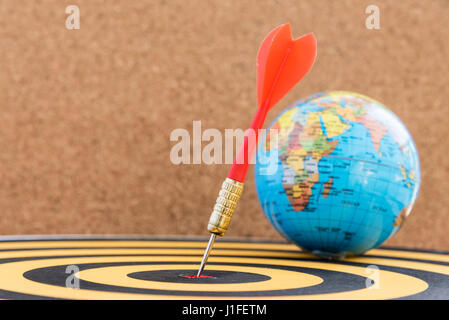 Freccia dardo colpendo in target bullseye di centro sul dartboard con globo e lo sfondo di legno con copia spazio, business marketing finanziario e educat Foto Stock