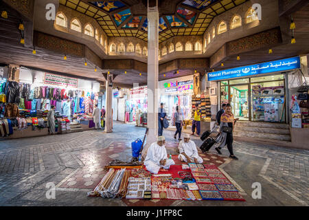 Muscat Oman - souk Muttrah uomini seduti sul tappeto in vendita sul mercato vari oggetti tradizionali Foto Stock