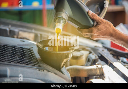 Auto manutenzione manutenzione meccanico versando olio nuovo lubrificante in il motore dell'auto, un meccanico si versa olio nuovo nel motore di una macchina come parte della sua maintena Foto Stock