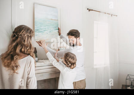 La famiglia felice appendere foto di mare oltre il camino a casa Foto Stock