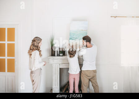 La famiglia felice appendere foto di mare oltre il camino a casa Foto Stock