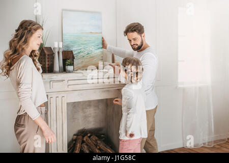 La famiglia felice appendere foto di mare oltre il camino a casa Foto Stock