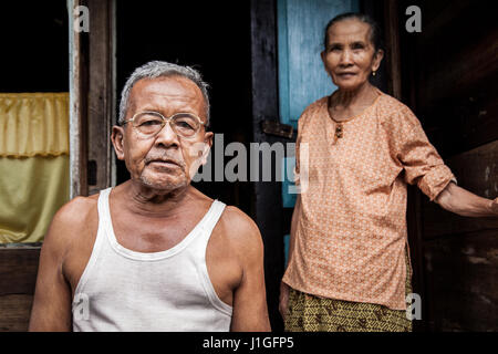 Anziani e umile giovane indonesiano, due anziani cercando deluso in piedi in ingresso alla loro povera e umile casa Foto Stock