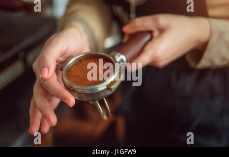 Primo piano della mano femminile con i baristi titolare con caffè appena macinato. Soft focus. Foto Stock