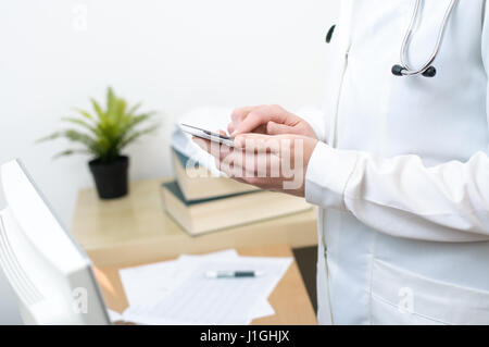 Un medico donna texting sullo smartphone in ufficio medico Foto Stock