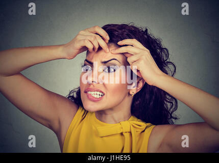 Closeup ritratto di una donna che guarda in uno specchio la spremitura di un acne o blackhead sulla sua faccia fronte Foto Stock