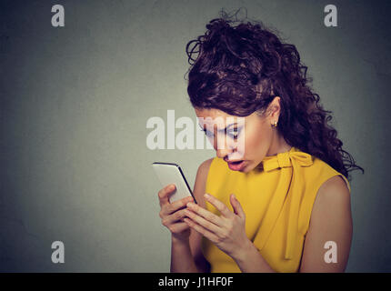 Spaventata scioccato giovane donna tenendo il cellulare in mani guardando lo schermo con la faccia trasversale di espressione in testi stressanti e chiamate isolate su backg grigio Foto Stock