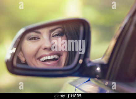 Felice giovane donna alla ricerca di driver in auto vista laterale specchio, assicurandosi che la corsia è libero prima di effettuare una svolta. Positivo volto umano Espressione di emozioni. Cassetta di sicurezza Foto Stock