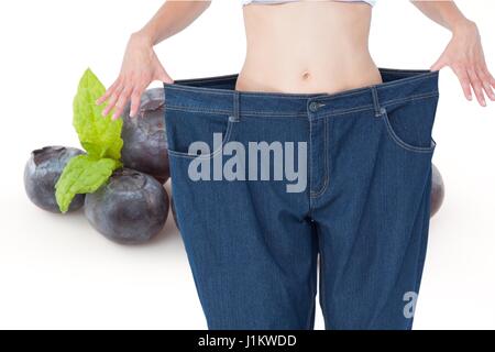 Composito Digitale della sezione mediana della donna in jeans allentati da mirtilli americani che rappresenta la perdita di peso concept Foto Stock