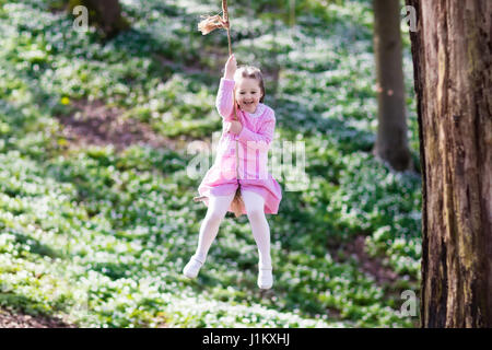 Carino bambina in abito rosa su albero swing corda in primavera in fiore giardino con fiori. Bambino oscillare all'aperto nel parco giochi del cortile. Bambini giocano ou Foto Stock