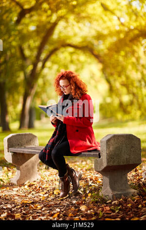 Redhead donna leggere il libro nel parco in autunno Foto Stock