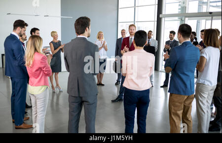 Giovane leader in piedi di fronte a i suoi partner che applaudire Foto Stock