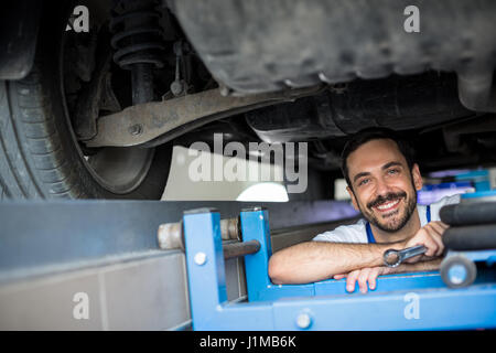 Maschio di lavoro meccanico sotto la vettura sorridente Foto Stock