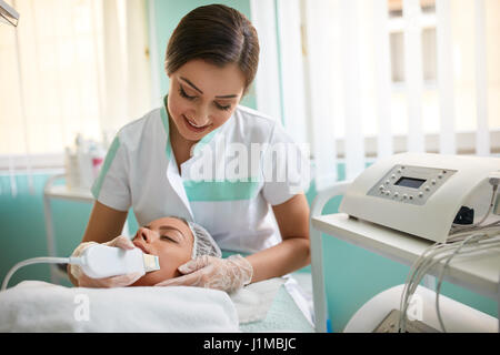 Donna di pulizia di ricezione la terapia con un professionista di apparecchiature ad ultrasuoni in cosmetologia clinica Foto Stock