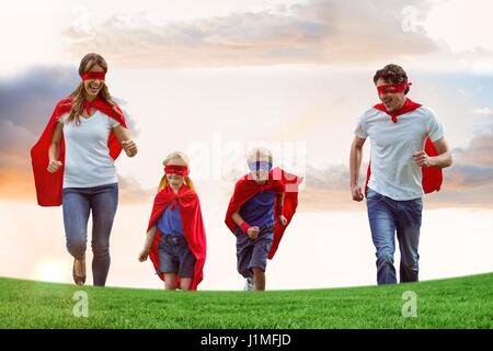 Composito Digitale della famiglia indossando mantelli e maschere per occhi durante il funzionamento sul campo contro sky Foto Stock