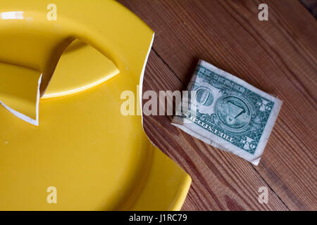 Rottura della piastra di colore giallo e un dollaro su sfondo di legno come un simbolo della crisi. Foto Stock