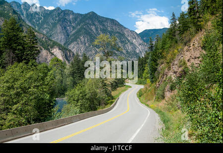 Un avvolgimento strada alberata passa un flusso e affioramenti rocciosi in salita attraverso le montagne a nord-est di Vancouver, Canada. Foto Stock