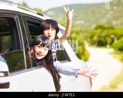 Felici i bambini asiatici sticking le loro teste fuori dal finestrino posteriore durante la guida di una vettura. Foto Stock