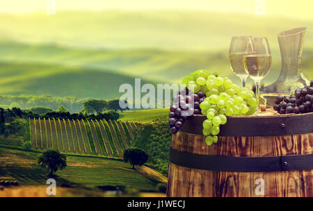 Vino bianco bottiglia e bicchiere di vino in botte barile. Bella Toscana sullo sfondo Foto Stock