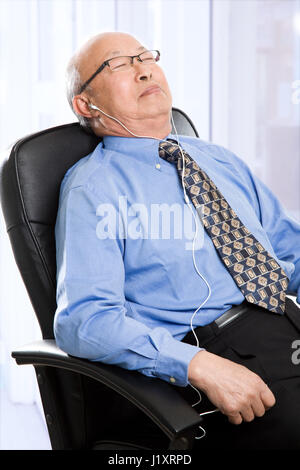 Un senior asian businessman dormendo e ascolto di musica in ufficio Foto Stock