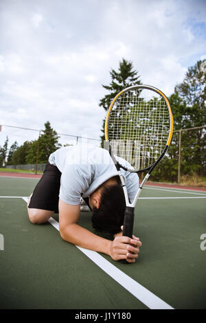 Un triste asian giocatore di tennis inginocchiati in delusione dopo la sconfitta Foto Stock
