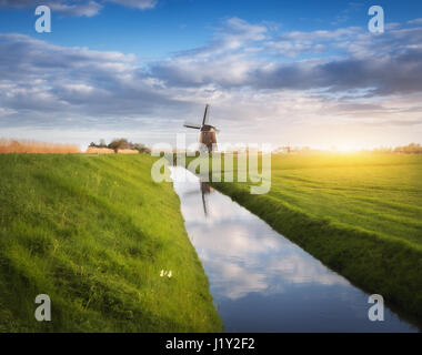 Mulini a vento di sunrise. Paesaggio agreste con mulini a vento olandese vicino all'acqua canali, erba verde e blu cielo nuvoloso riflessa nell'acqua. Mattina di sole Foto Stock