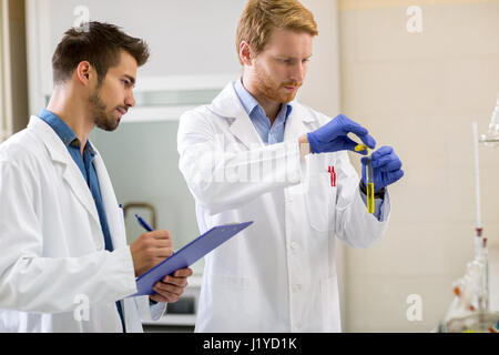 Tecnico di laboratorio miscelazione liquidi in laboratorio assistente durante la scrittura dei dati Foto Stock